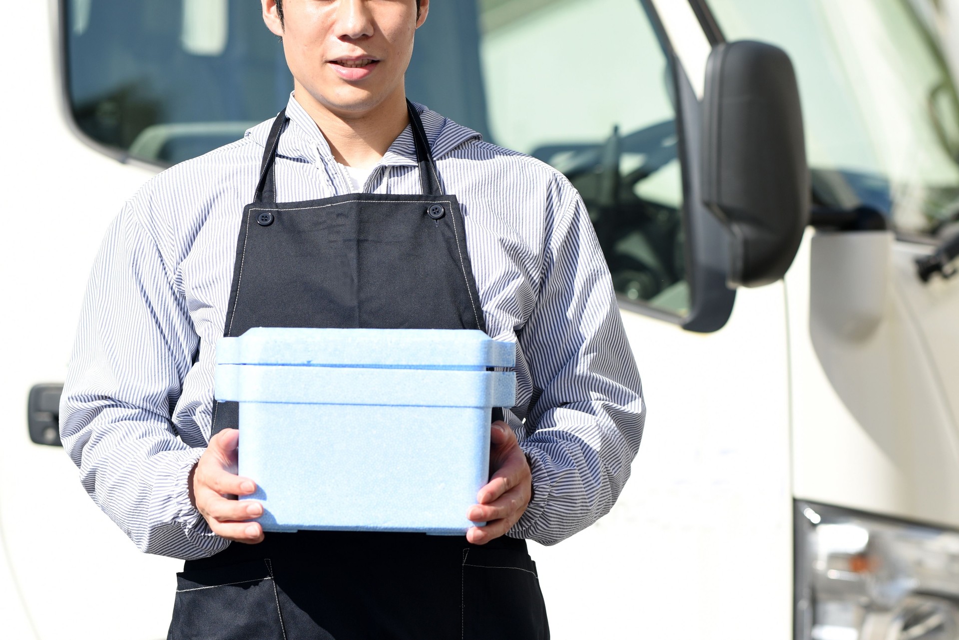 Asian male delivery man holding a cooler box in front of the truck